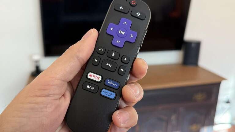 Roku remote in hand in front of a TV set