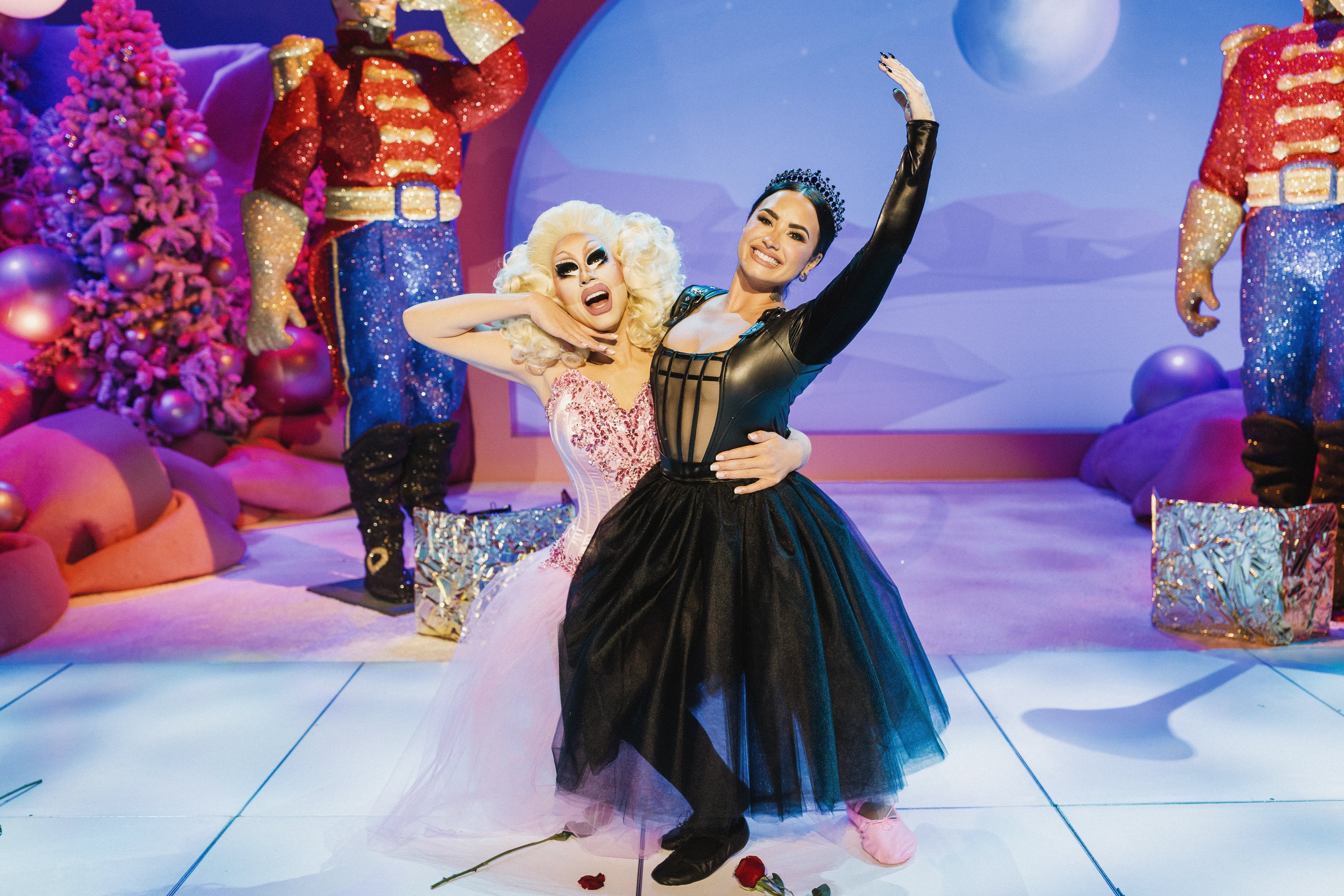 Drag queen Trixie Mattel in a pink ballet costume with her arm wrapped around Demi Lovato, dressed in a black ballet costume on a "Nutcracker"-themed set for the Roku Original special "A Very Demi Holiday Special"