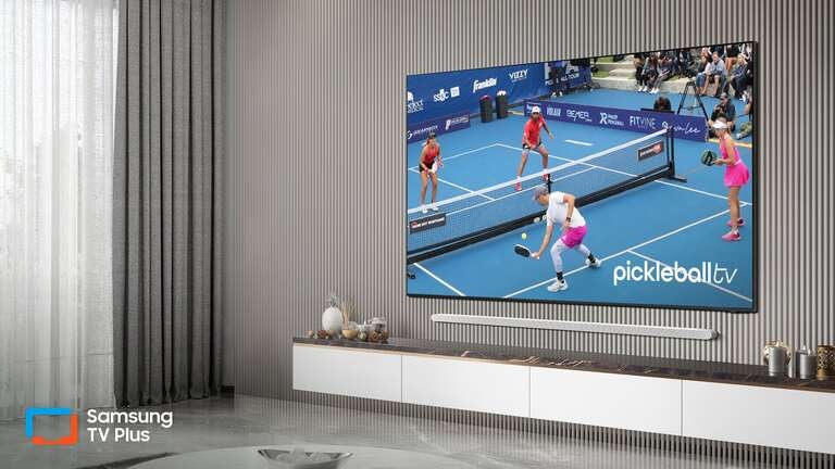 A flatscreen TV displaying PickelballTV featuring four pickleball players in action is mounted on a wall in a gray living room