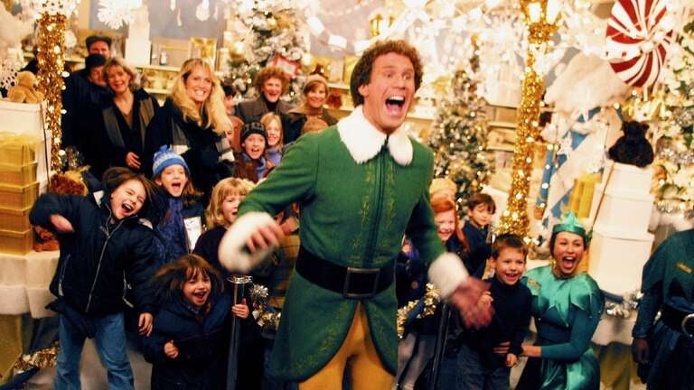 Will Ferrell in costume as Buddy the Elf with a background cast of children in "Elf"