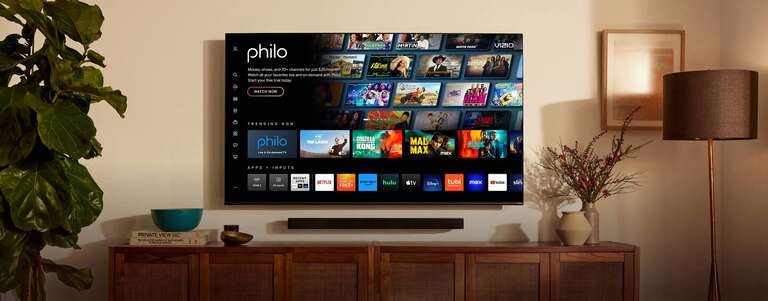 A flat screen TV displaying Philo's home interface is mounted on wall above a wooden TV center