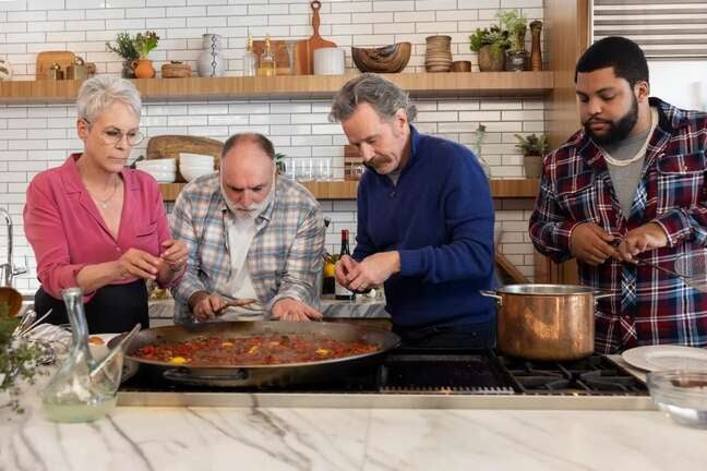Jamie Lee Curtis, José Andrés, Bryan Cranston, and O’Shea Jackson Jr. stand together in a kitchen over a cooking range, focused while preparing a dish